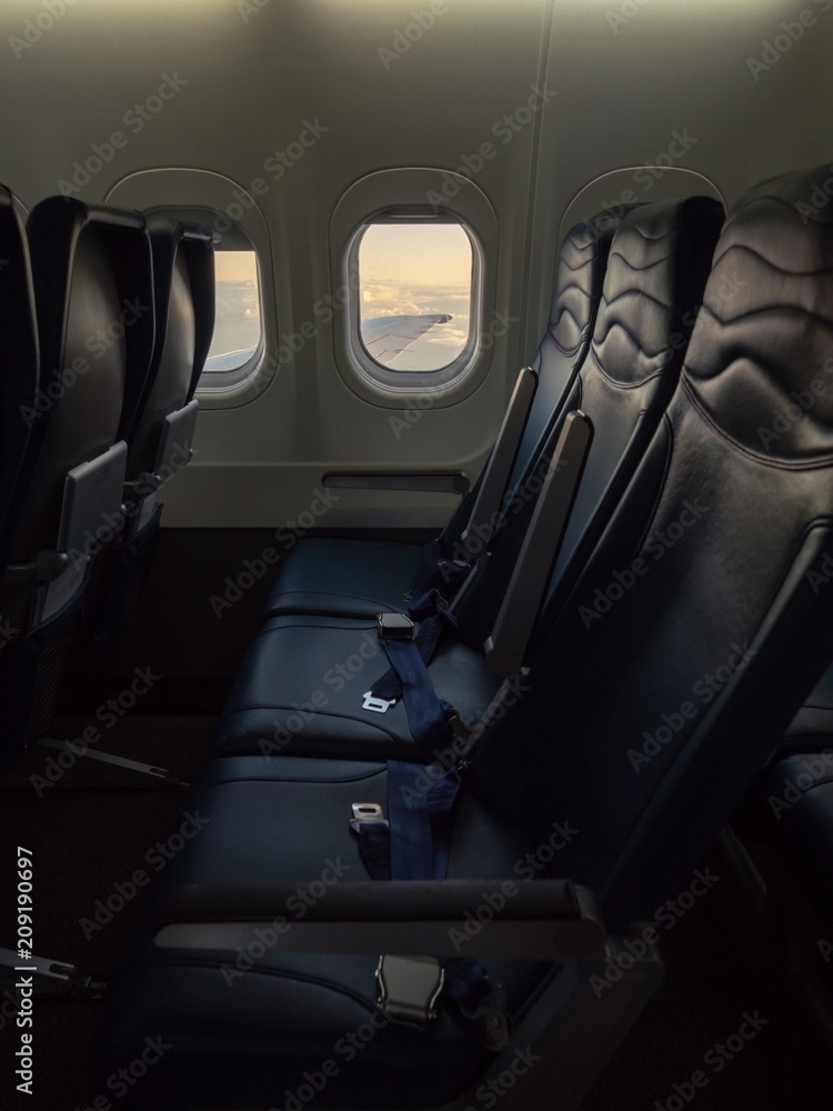 Empty three sites inside a flying airplane with wing and clouds view from window