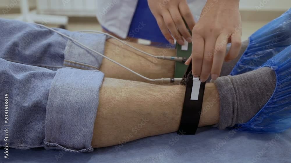 Doctor put electrodes on legs of senior man Doctor put electrodes on legs of senior man