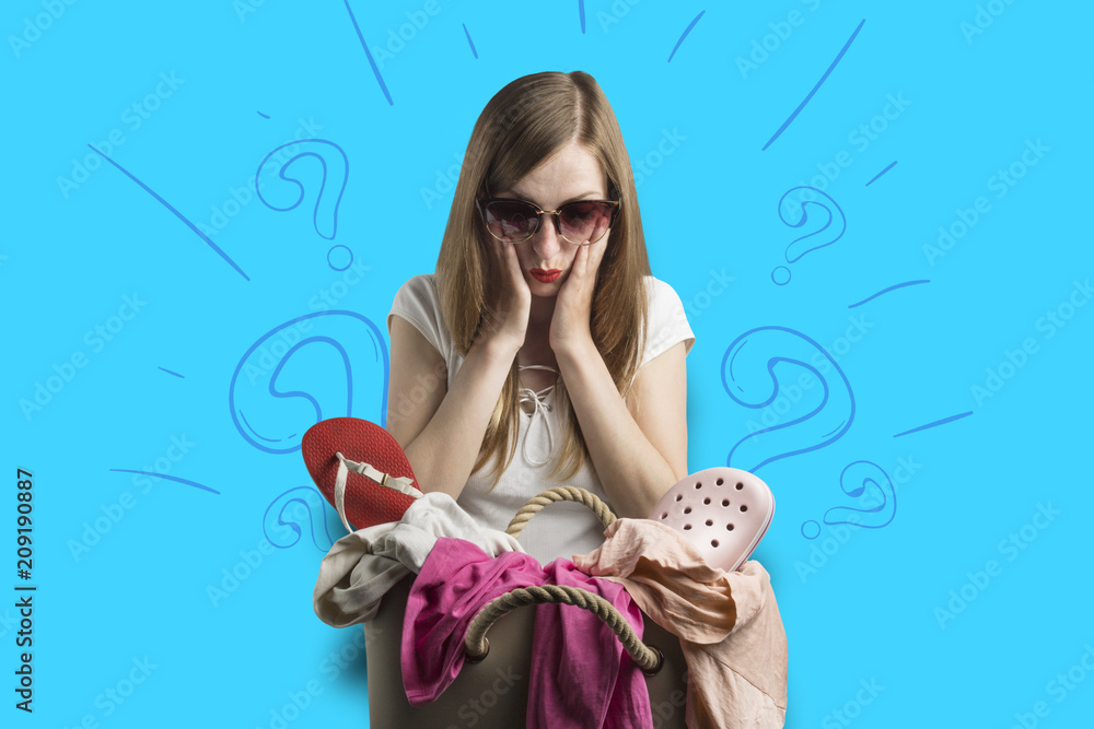 young girl is looking at a bag full of clothes on a blue background with question marks. Concept of fees for travel and crowded baggage young girl is looking at a bag full of clothes on a blue background with question marks. Concept of fees for travel and crowded baggage