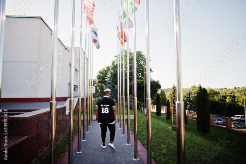 Stylish arabian muslim boy with originally hair posed on streets, against flags of different countries.