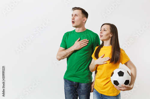 Obraz na plátně Emotional couple, woman man, football fans in yellow green t-shirt cheer up support team with soccer ball singing national country anthem isolated on white background