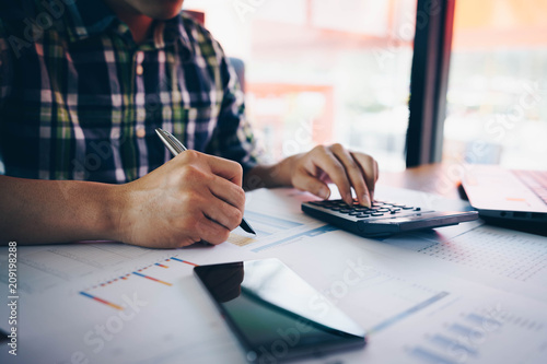 Businessman or accountant hand holding pen working with calculator and laptop computer for business financial document report, Business financial and accounting concept