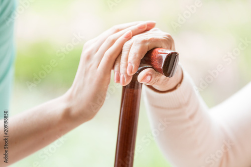 Close-up of caregiver holding hand on hand of senior person with walking stick