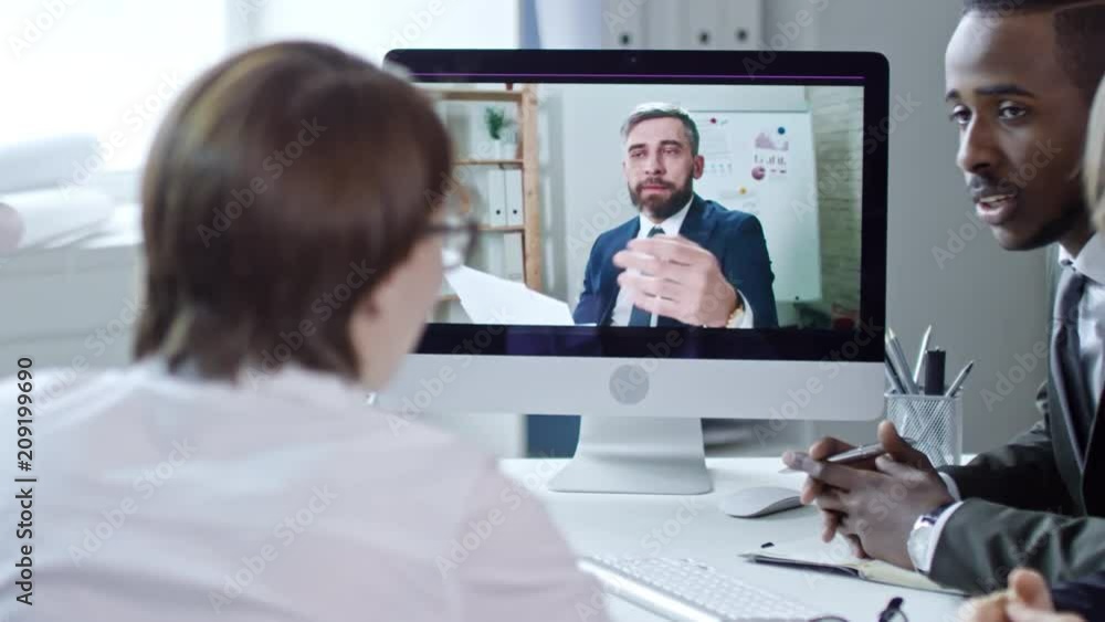 Tracking of mid-aged businessman showing documents at web cam and speaking with multiethnic team while having web conference in the office Tracking of mid-aged businessman showing documents at web cam and speaking with multiethnic team while having web conference in the office