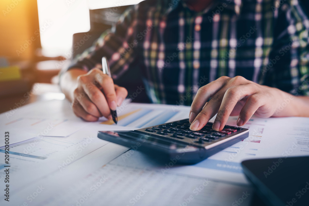 Businessman or accountant hand holding pen working with calculator and laptop computer for business financial document report, Business financial and accounting concept Businessman or accountant hand holding pen working with calculator and laptop computer for business financial document report, Business financial and accounting concept