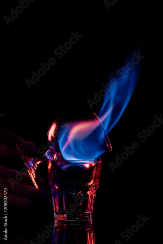 partial view of woman holding glass with burning sambuca alcohol drink on black background