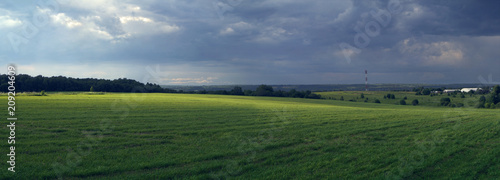 Rural panoramic landscape with sun-lit fielda field  before a thunder-storm.