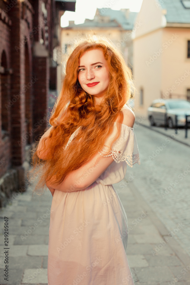 Smiling ginger model with long hair wearing white dress with naked shoulders Smiling ginger model with long hair wearing white dress with naked shoulders