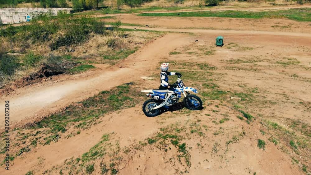 Equipped rider is standing with his motorbike in the middle of an outdoor track Equipped rider is standing with his motorbike in the middle of an outdoor track