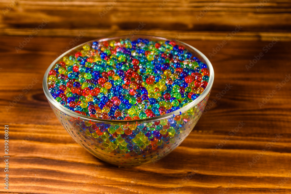 Multicolored hydrogel balls in a glass bowl on wooden table Multicolored hydrogel balls in a glass bowl on wooden table