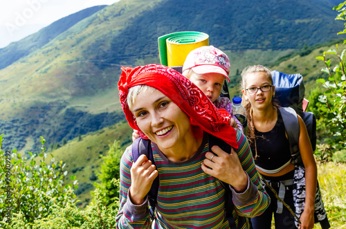 Young happy mother hold little traveller on back - baby girl in carrying backpack enjoying travel adventure, Hiking activity with child on family summer vacation, weekend nature tour