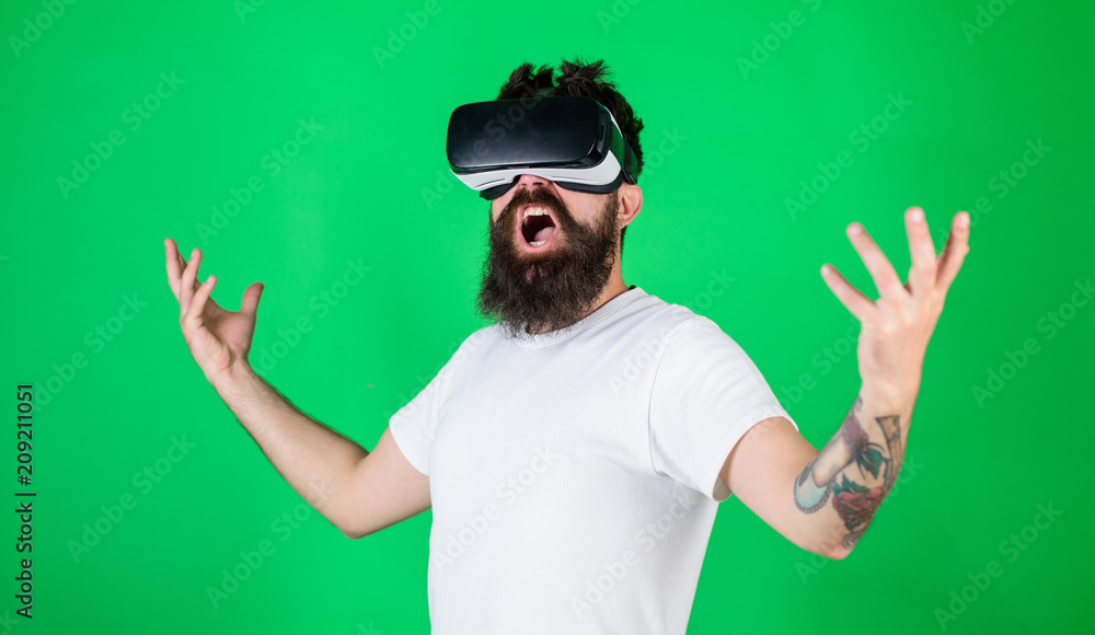 Guy with head mounted display interact in VR. Man with beard in VR glasses, green background. Power concept. Hipster on shouting face raising hands powerfully while interact in virtual reality Guy with head mounted display interact in VR. Man with beard in VR glasses, green background. Power concept. Hipster on shouting face raising hands powerfully while interact in virtual reality