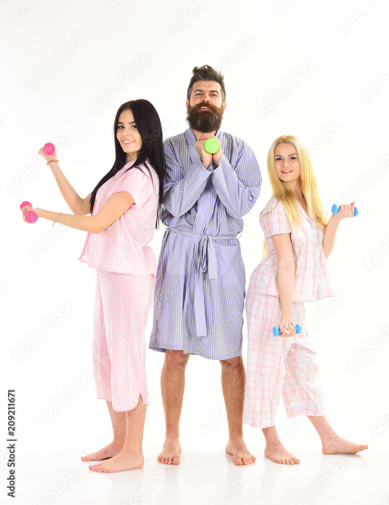 Bearded man with sporty ladies. Trainer, macho with attractive girls do morning exercises. Fitness morning concept. Company of friends with dumbbells in domestic clothes, isolated on white background. Bearded man with sporty ladies. Trainer, macho with attractive girls do morning exercises. Fitness morning concept. Company of friends with dumbbells in domestic clothes, isolated on white background.