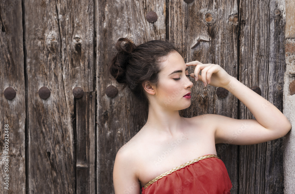 Fototapeta premium Portrait of a girl in red dress on a wooden door