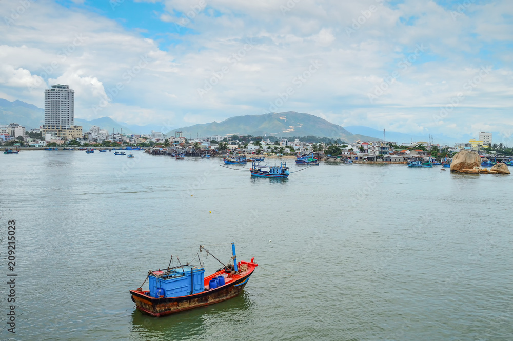Fototapeta premium fishing schooners in the parking lot, in the riverbed of the Kai River, on the background buildings, mountains, and the sky covered with clouds, Nha Trang, Vietnam