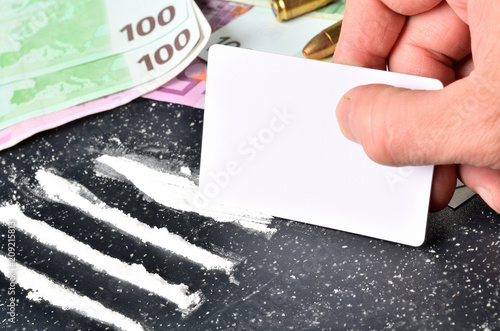 Close-up of hand making cocaine lines using a white card, euro banknotes money in background