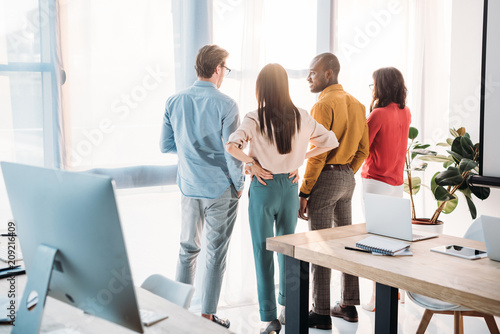Photography back view of multiethnic business colleagues looking out window in office