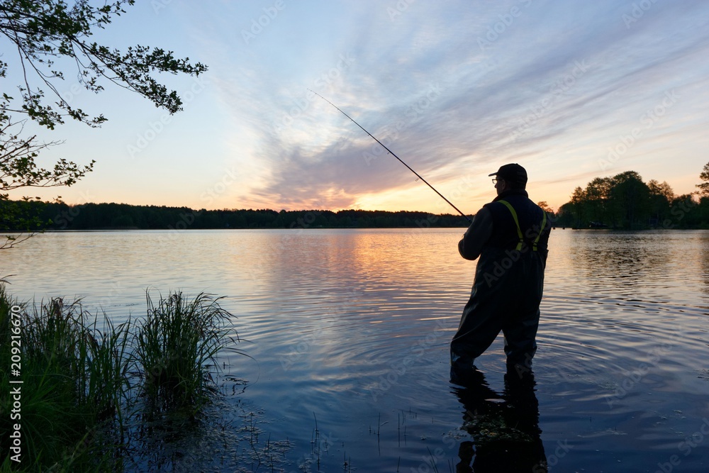 Silhouette of fisherman standing in the lake and catching the fish during sunrise
