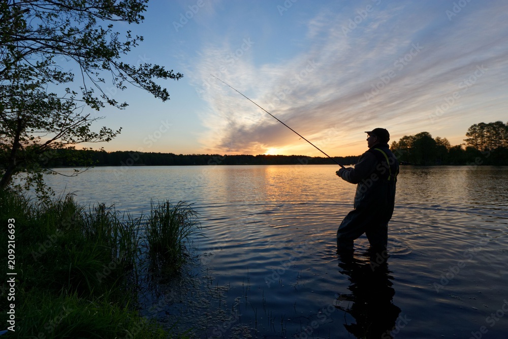 Silhouette of fisherman standing in the lake and catching the fish during sunrise
