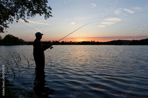 Silhouette of fisherman standing in the lake and catching the fish during sunset