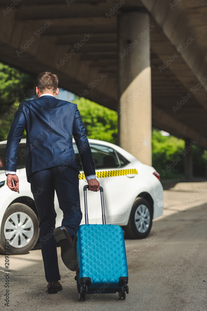 back view of stylish young man with suitcase running to taxi back view of stylish young man with suitcase running to taxi