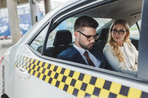 young couple in formal wear and eyeglasses sitting together in taxi