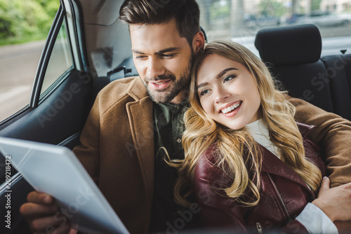 smiling young couple using digital tablet while sitting together in car