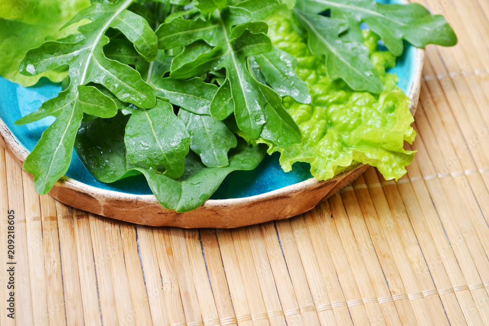 Summer green vegetables spinach arugula salad in blue plate on wooden surface Summer green vegetables spinach arugula salad in blue plate on wooden surface