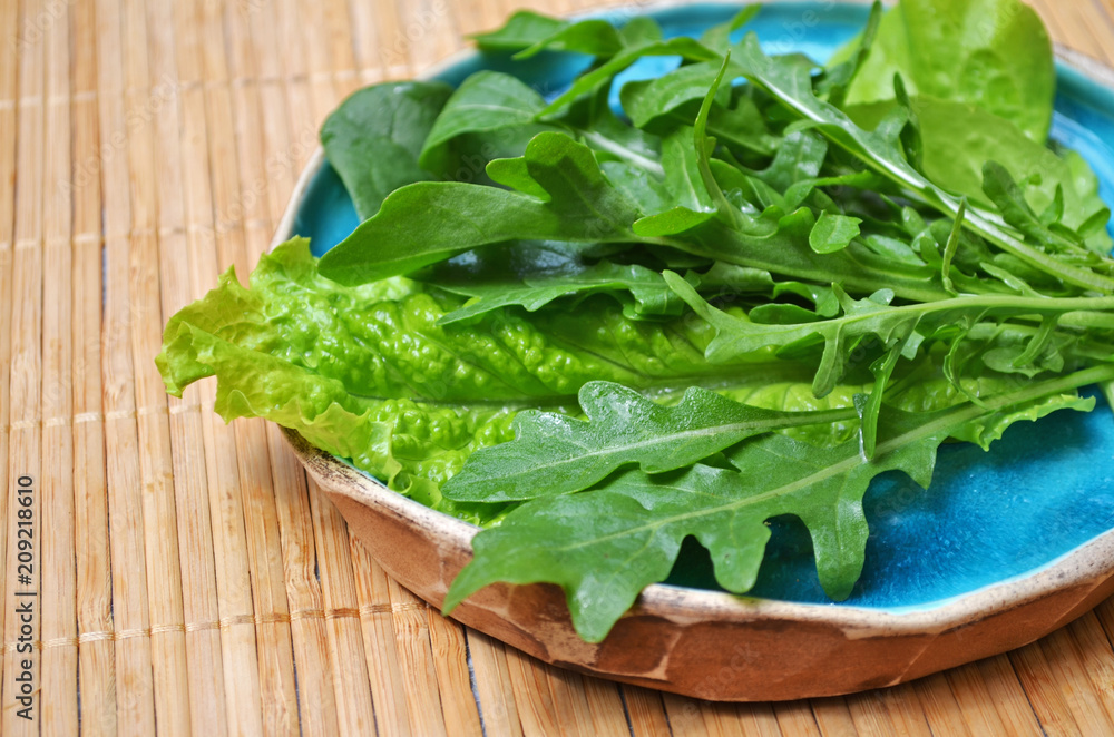 Summer green vegetables salad arugula spinach in blue plate on wooden surface Summer green vegetables salad arugula spinach in blue plate on wooden surface
