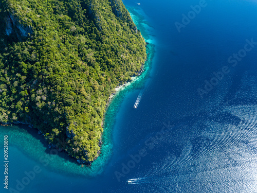 Aerial drone view down onto boats over a tropical coral reef surrounded by mountains and jungle