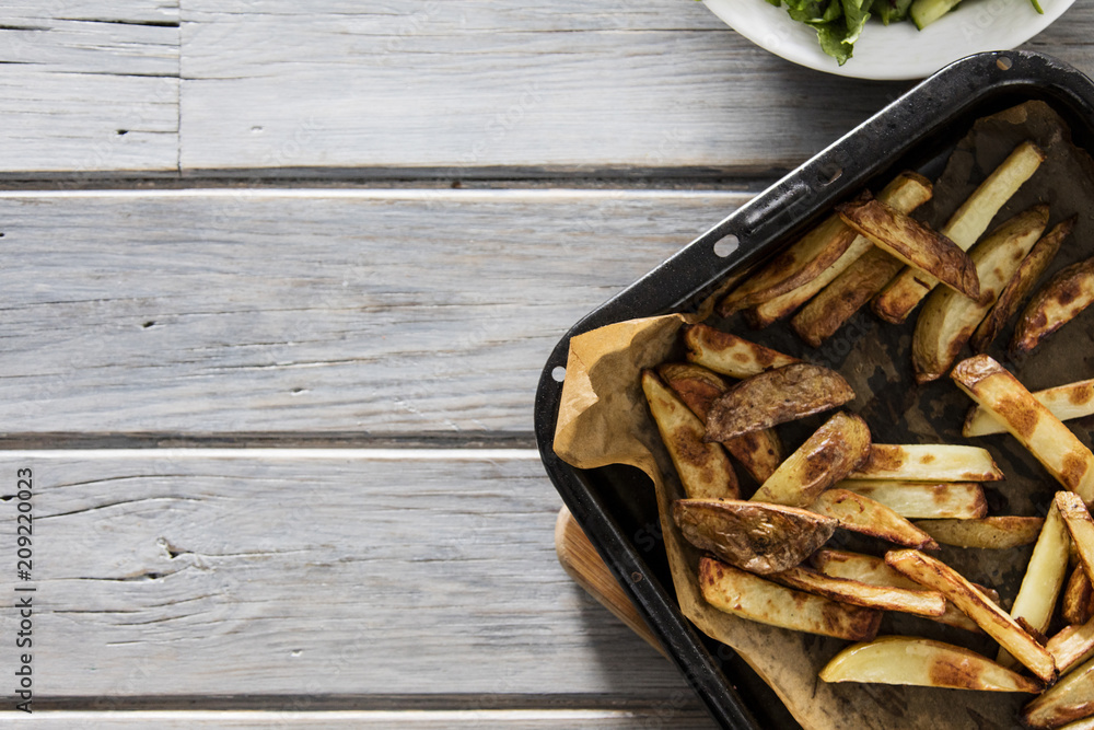 Homemade baked skin on potato fries on a rustic wooden background