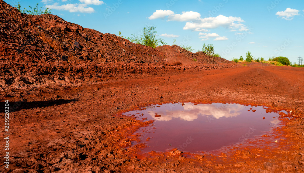 Φωτογραφία Reflection of the clouds in small puddle on dry red soil in Kryvyi Rih, Ukraine