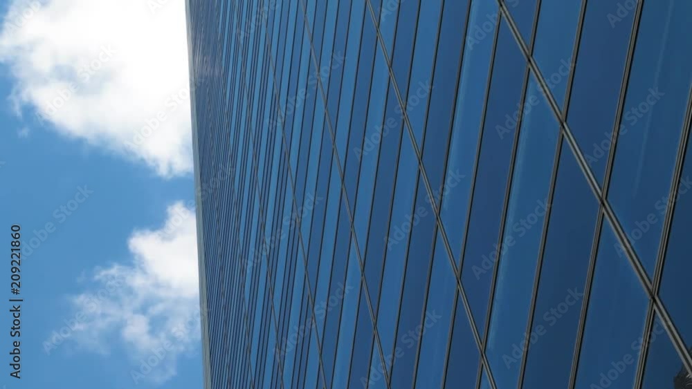 Glass facade of skyscraper building against gray blue sky and running clouds. Concept of business, global finance, economy and communication. Glass facade of skyscraper building against gray blue sky and running clouds. Concept of business, global finance, economy and communication.