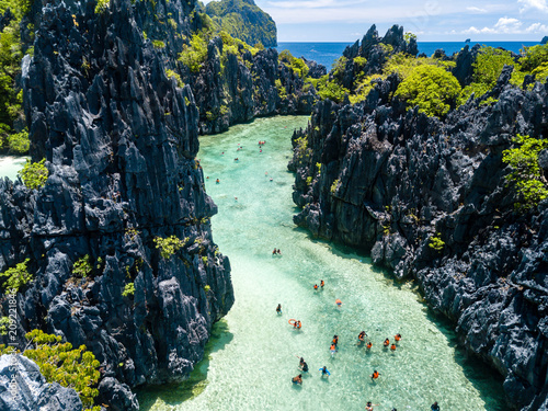 Aerial drone view of swimmers and tourists inside a beautiful, shallow tropical laggon surrounded by jagged cliffs photo