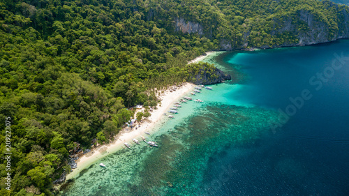 Aerial drone view of traditional Banca boats and coral reef surrounding a scenic tropical sandy beach (7 Commando Beach, El Nido)