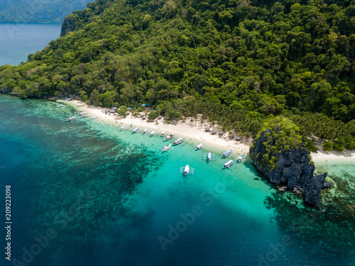 Aerial drone view of traditional Banca boats and coral reef surrounding a scenic tropical sandy beach (7 Commando Beach, El Nido)