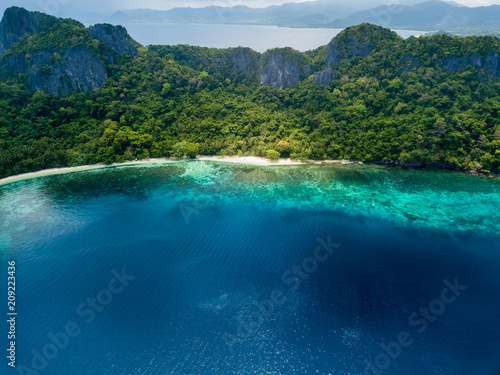 Aerial drone view of a beautiful deserted tropical beach surrounded by large cliffs and jungle (Cadlao Island, El Nido, Palawan)