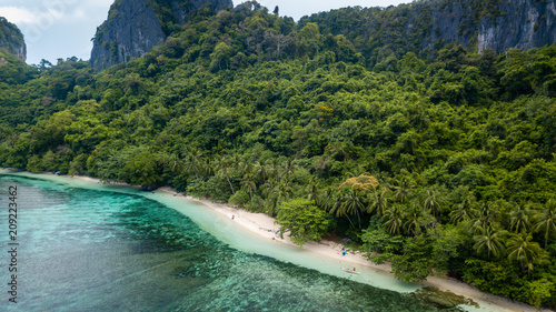 Aerial drone view of a beautiful deserted tropical beach surrounded by large cliffs and jungle (Cadlao Island, El Nido, Palawan)