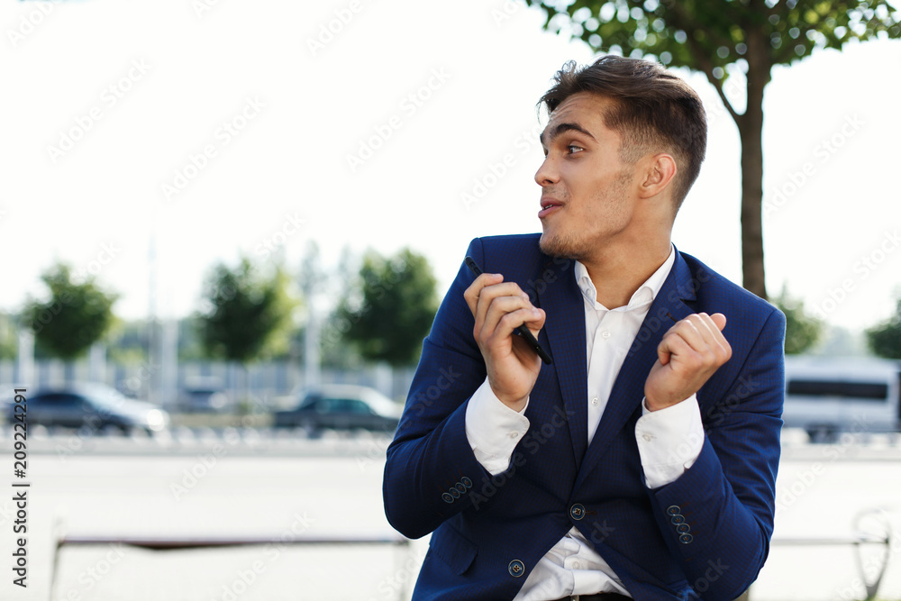 Happy young businessman holds smartphone in his arm and screams sitting on the street Happy young businessman holds smartphone in his arm and screams sitting on the street