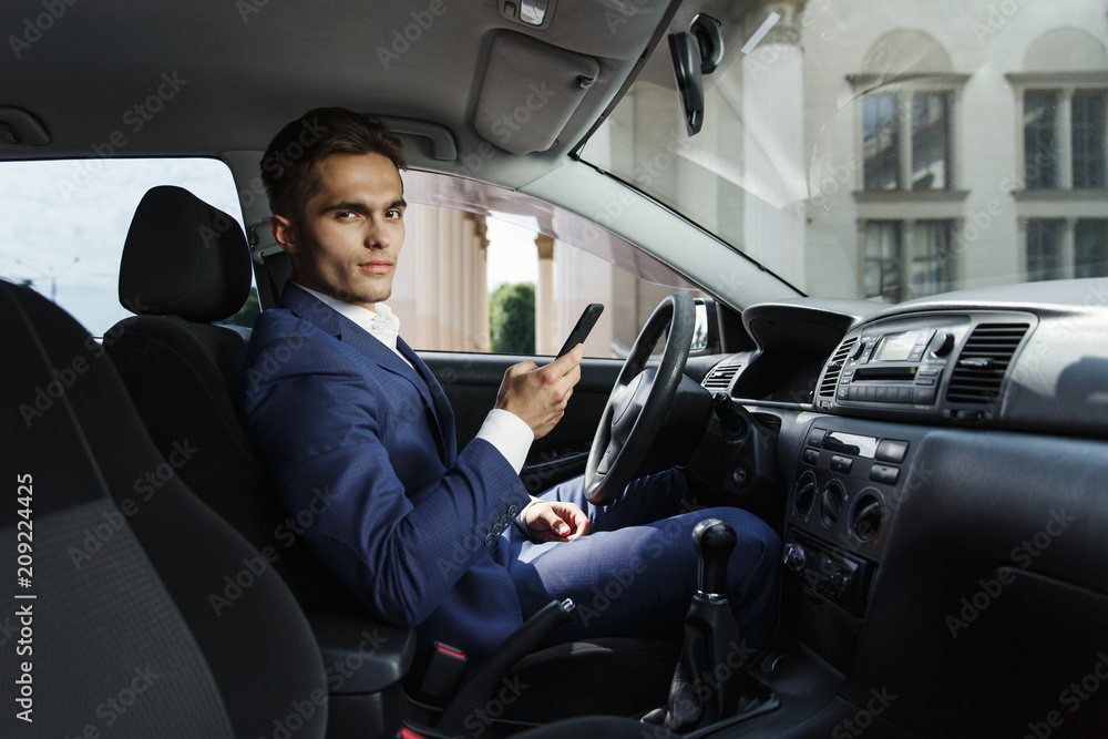 Smiling businessman sits insde the car and works with his smartphone Smiling businessman sits insde the car and works with his smartphone