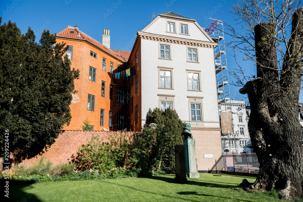 sculpture between green trees and bushes, brick wall and houses in copenhagen, denmark