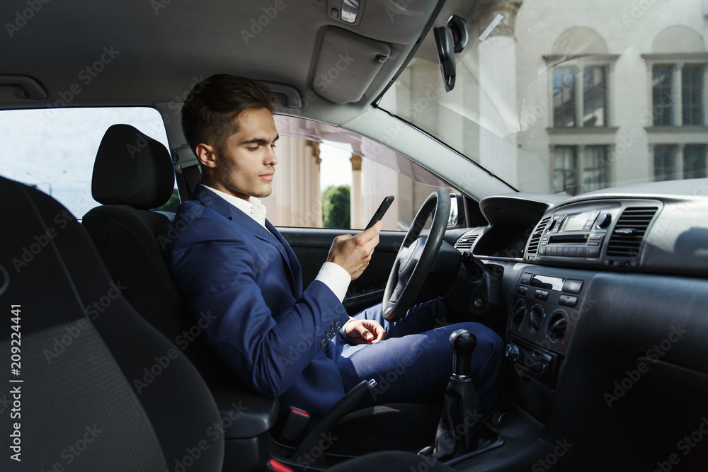 Smiling businessman sits insde the car and works with his smartphone Smiling businessman sits insde the car and works with his smartphone
