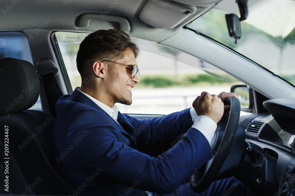 Happy businessman sits shows his emotions sitting at the steering wheel inside the car Happy businessman sits shows his emotions sitting at the steering wheel inside the car