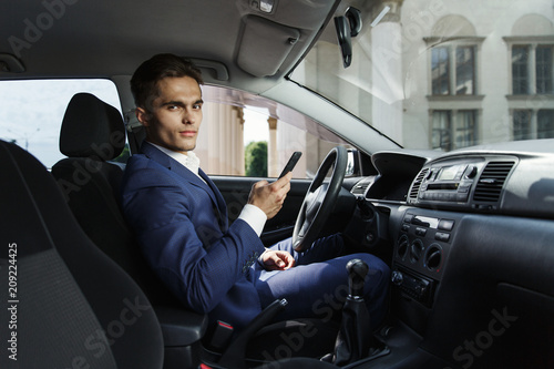 Smiling businessman sits insde the car and works with his smartphone © IVASHstudio