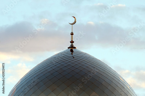 The symbol of Islam is a golden crescent moon on top of the mosque. Minaret on the blue evening of the morning sky with clouds.