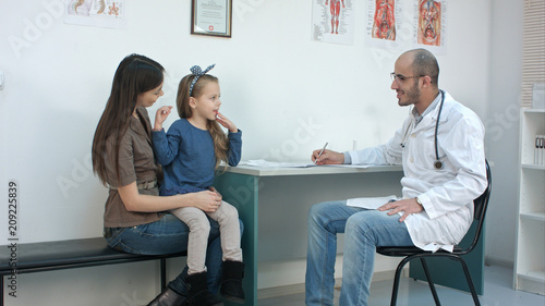 Smiling male doctor talking with shy little girl sitting on her mom laps