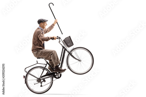 Joyful senior with a cane riding a bicycle and doing a wheelie