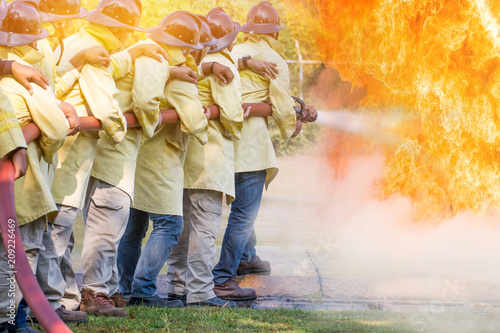 Firemen using water from hose for fire fighting at fire fight training of insurance group.Firefighter wearing a fire suit for safety under the danger training case.