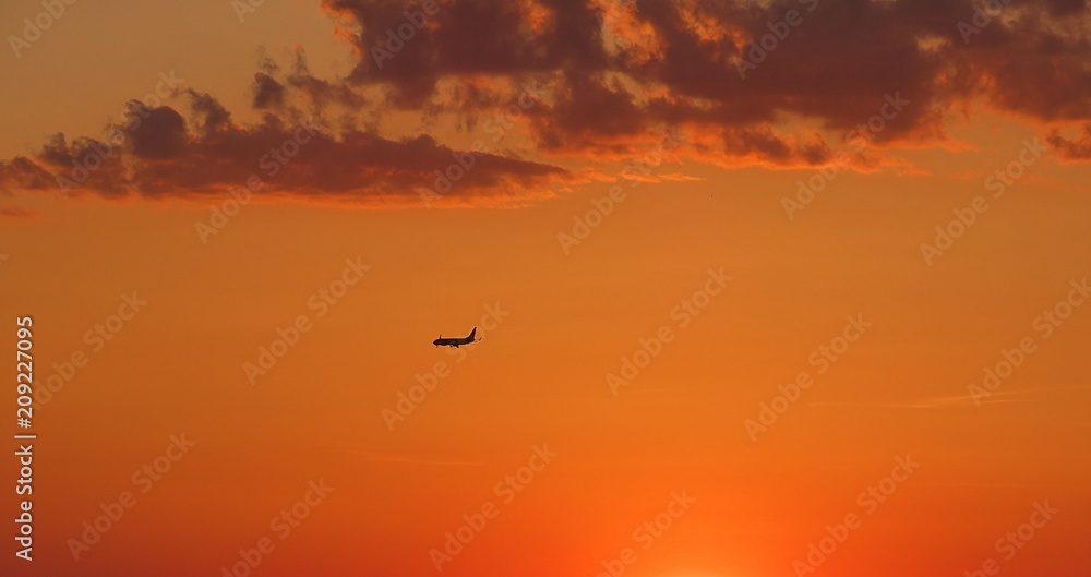 Airplane on beautiful fiery orange sunset background in the sky Airplane on beautiful fiery orange sunset background in the sky