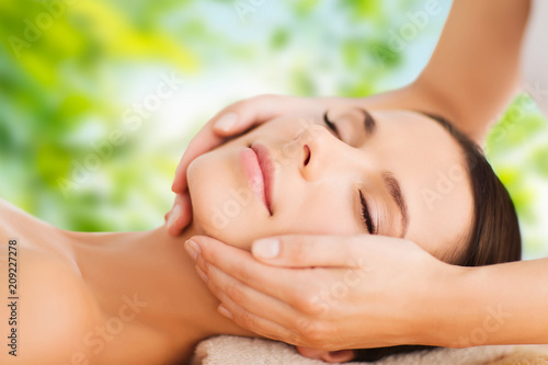 wellness  spa and beauty concept - close up of beautiful woman having face massage over green natural background
